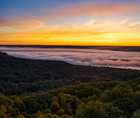 Sunrise over forested hills and a misty valley, with orange and blue sky.