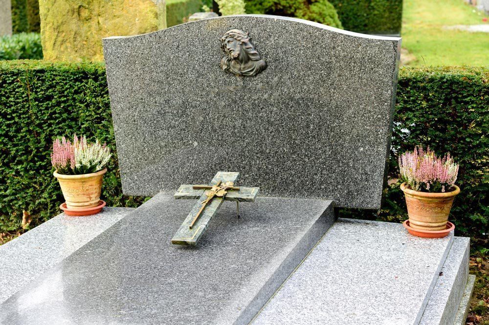 Una tomba con una croce e dei fiori sopra in un cimitero.