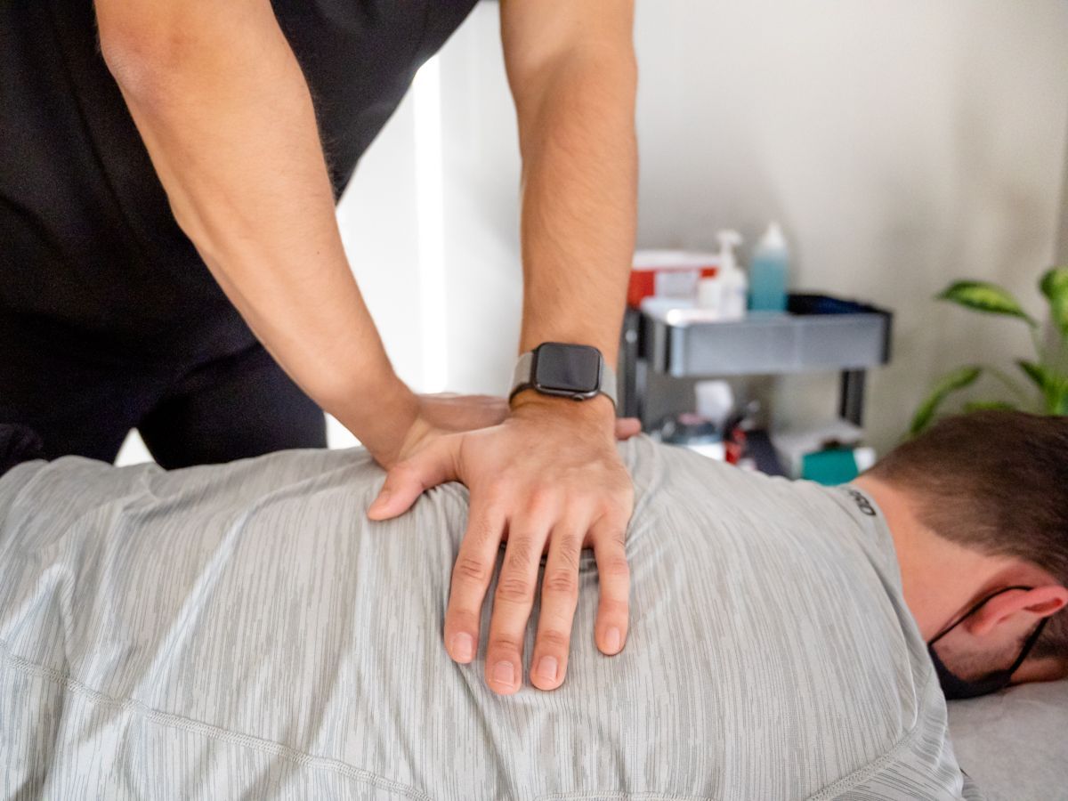 A massage therapist performing manual therapy on a person's upper back in a clinical setting.