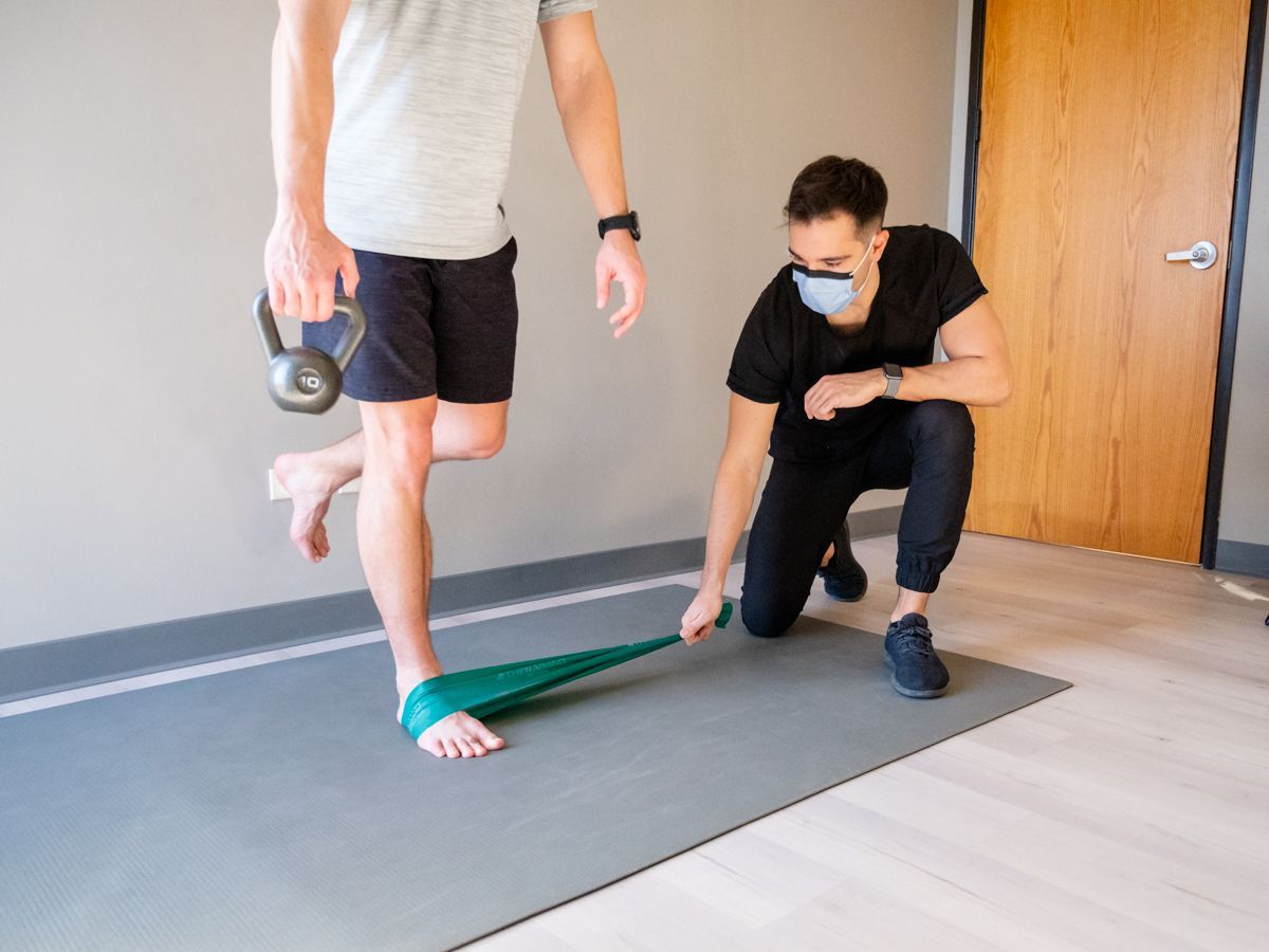 a man wearing a mask is helping another man with a resistance band .
