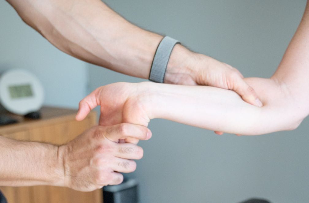 A physical therapist performs an assessment or manual therapy on a patient's wrist and forearm in a clinical setting.