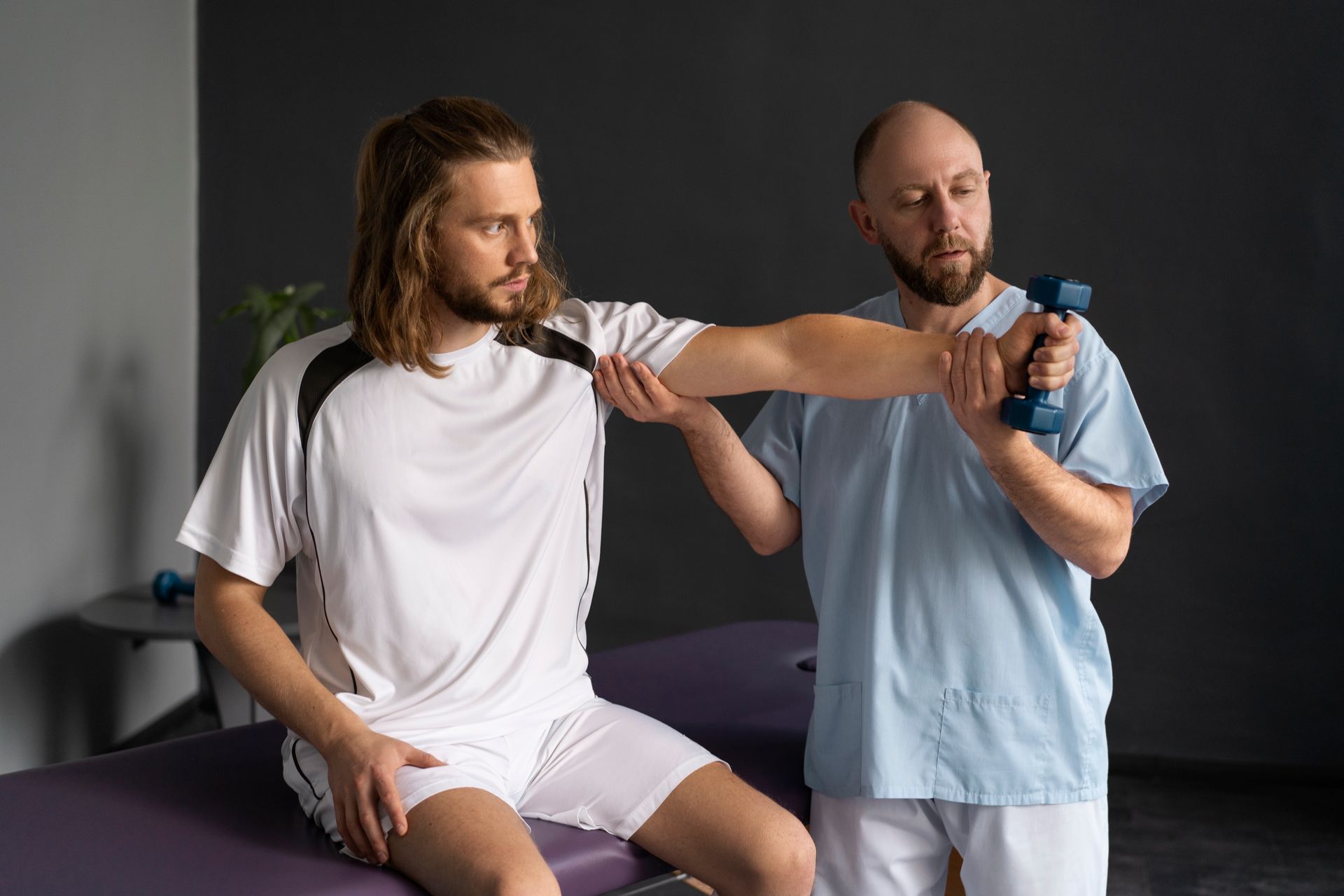a man is sitting on a table while a man is holding a dumbbell .