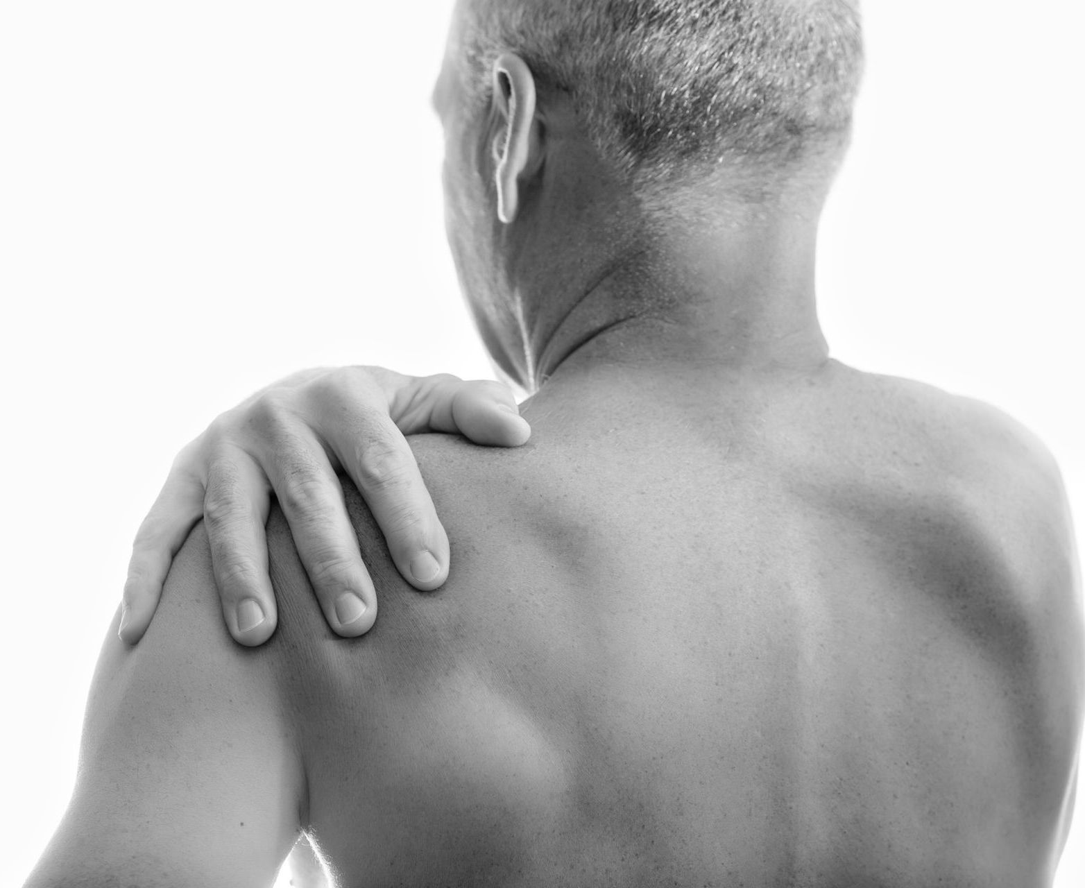 A person with their hand on their shoulder, suggesting pain or discomfort.