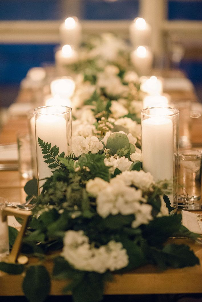 Table setting with white flowers, greenery, and candles, creating a warm, inviting ambiance.