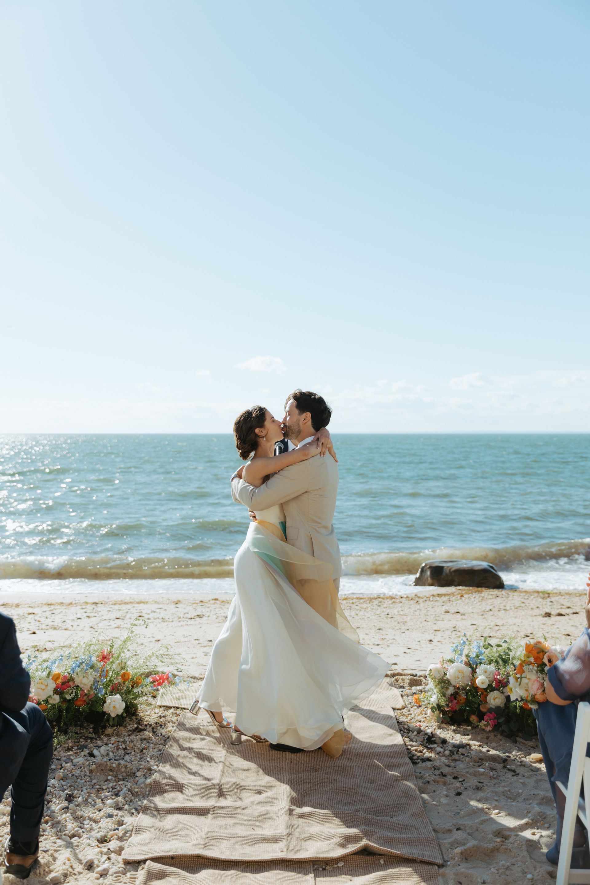 Couple embracing and kissing on a sunny beach after getting married.