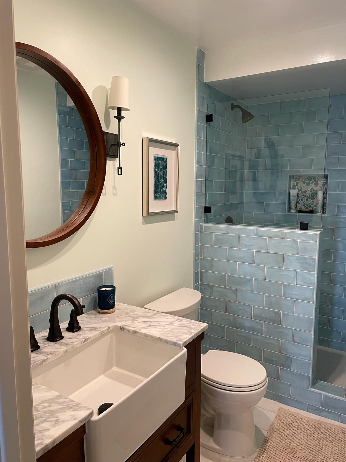 Bathroom with blue tile shower, white sink, round mirror, and mint-green walls.