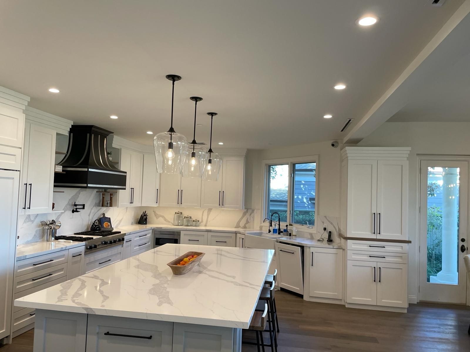 White kitchen with island, marble countertops, black range hood, and pendant lights.