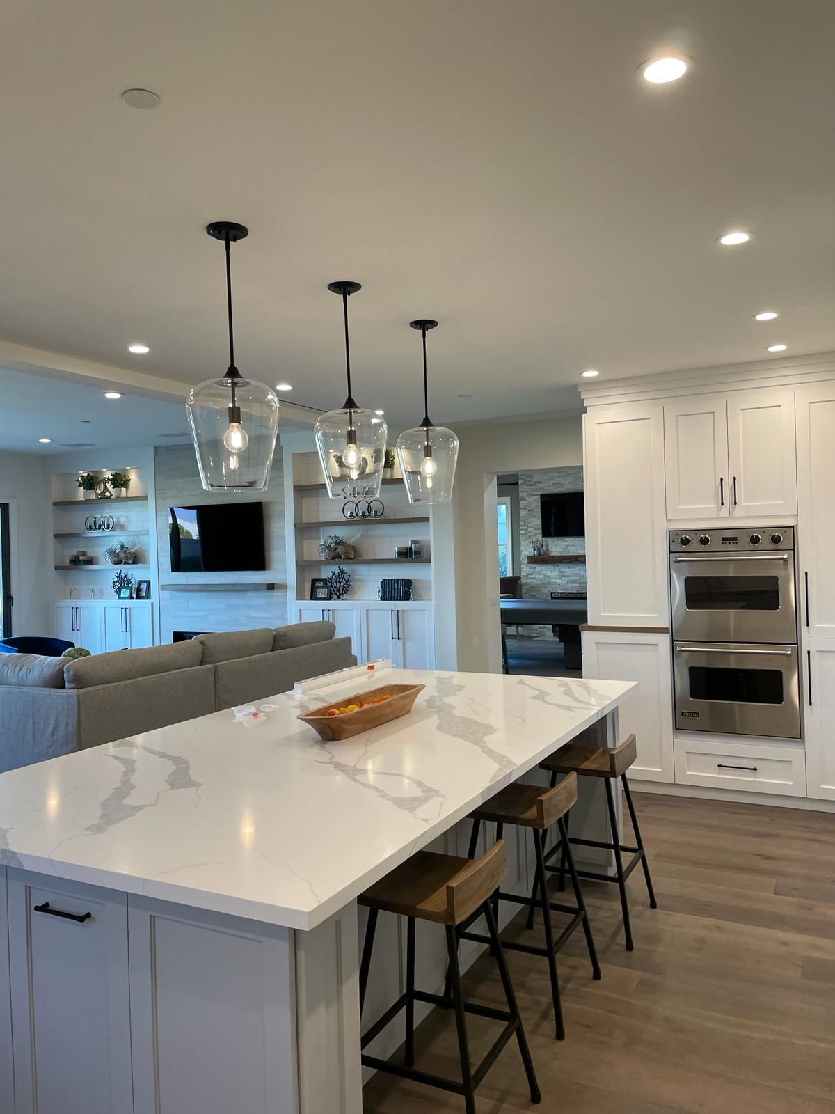 Modern kitchen with a white island, three pendant lights, and built-in ovens.