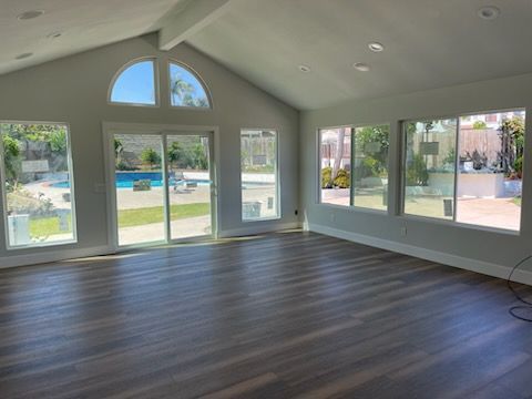 Empty room with gray walls, dark wood floor, and large windows overlooking a pool and yard.