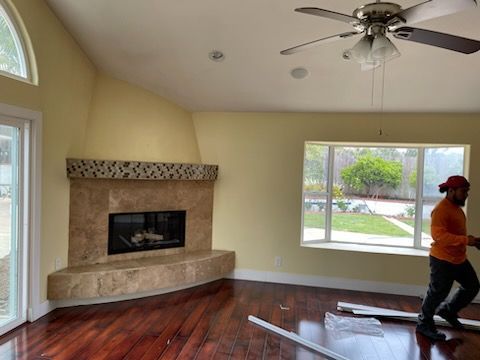 Living room with fireplace, hardwood floor, window, and a person walking with supplies.