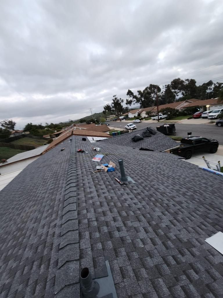 Roof of a house with gray shingles under a cloudy sky, showing surrounding neighborhood.