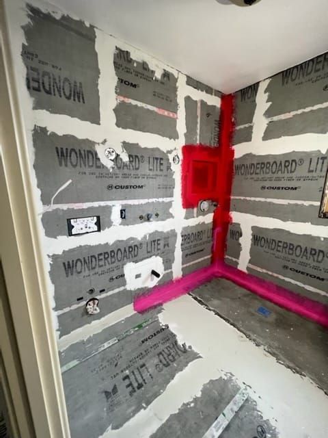 Shower construction with gray wallboard, pink waterproofing, and concrete corners.