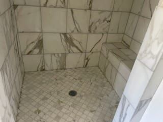 Shower with white marble tiles and built-in bench. Diagonal tile flooring leads to a drain.