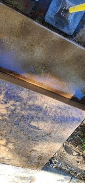 Close-up of a weathered, angled metal surface with blue and brown tones, possibly a construction site.