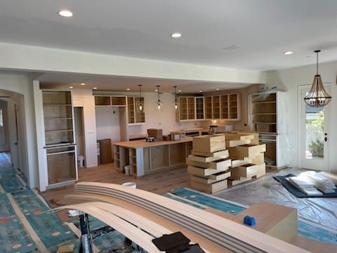 Kitchen under construction: cabinets, island, boxes, open space, overhead lights, and a doorway to the exterior.