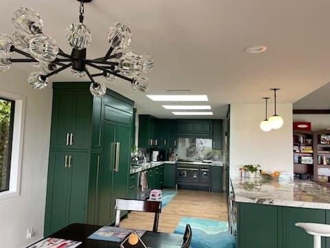 Emerald green kitchen with large cabinets, central chandelier, and a stove.