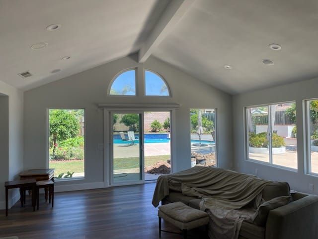 Bright living room with pool view, arched window, sliding glass door, white walls, and wood floor.