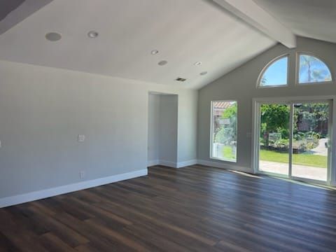 Empty living room with wood floor, white walls and vaulted ceiling, large windows.