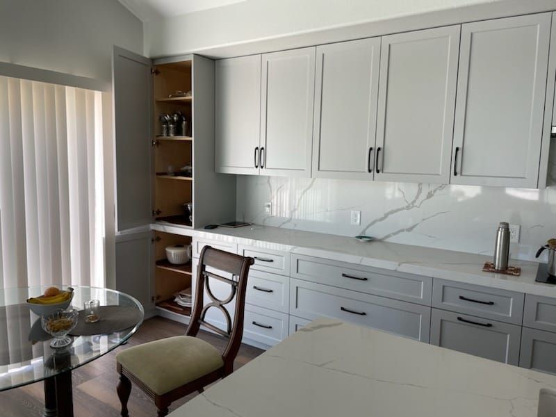 Modern kitchen with gray cabinets, marble backsplash, and a glass-top table with a chair.