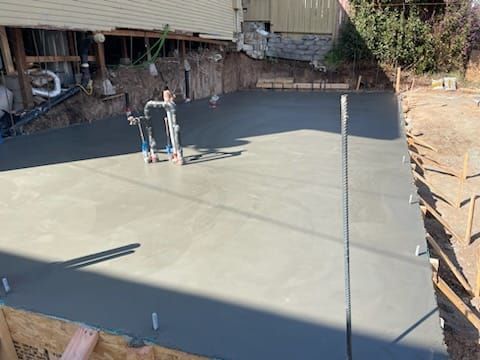 Freshly poured concrete slab in an excavated area, with finishing tools and wooden forms.