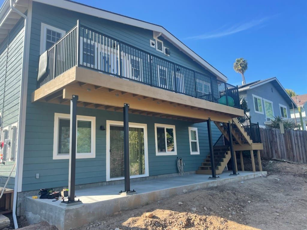 Deck addition on a blue house with black railings, supported by black posts, over a concrete patio.