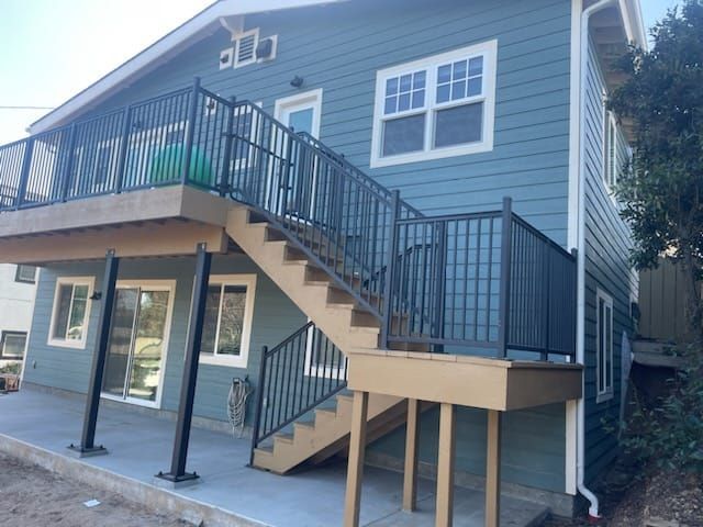 Two-story house with blue siding and exterior staircase leading to a deck. Black railings.