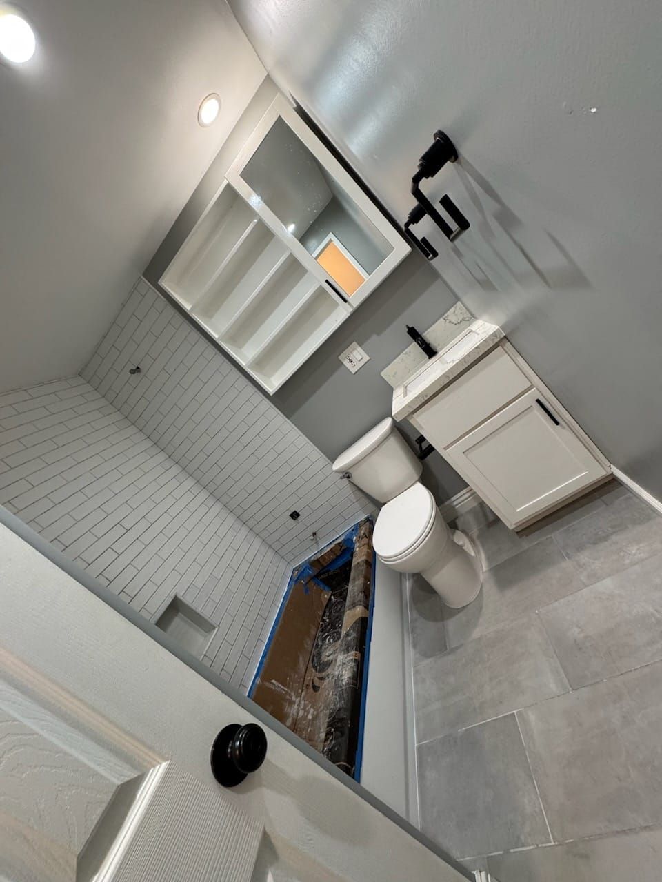 A newly renovated bathroom with white and gray tones. Features a toilet, vanity, and built-in shelving.