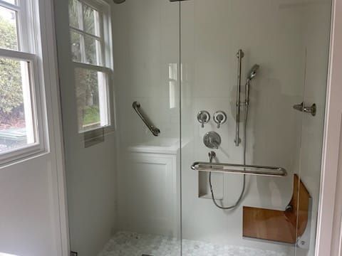 Walk-in shower with glass doors and grab bars. Features a small sink and window.