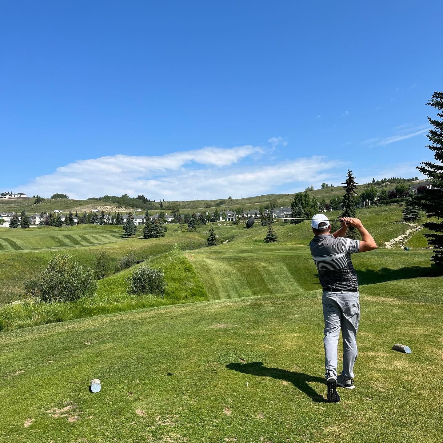 Golfer tees off on a sunny day at a golf course. Lush green fairways and blue sky.