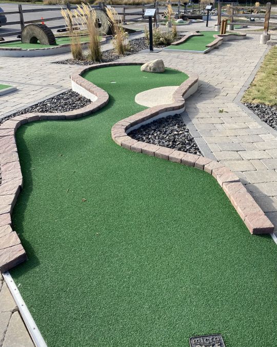 Miniature golf course with green turf, brick borders, and cobblestone path.