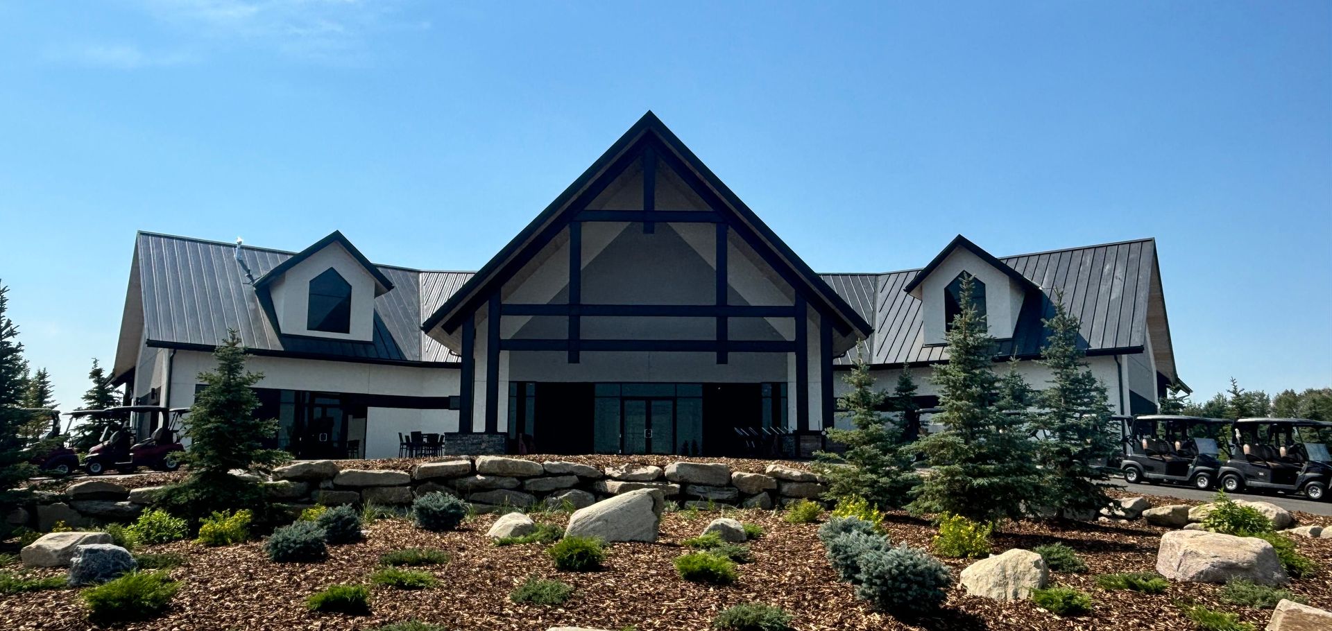 Exterior of a modern, white building with black trim, a large central gable, and trees under a blue sky.