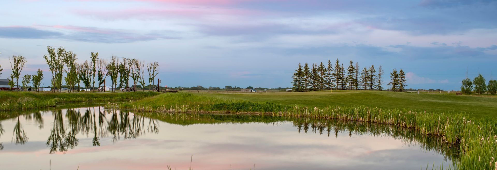 A tranquil wetland landscape with a reflecting pond and green fields under a cloudy sky.