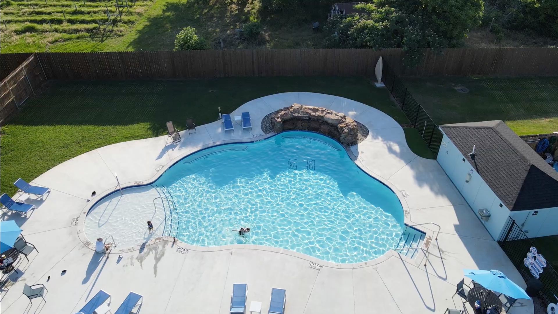Aerial view of a backyard swimming pool with lounge chairs, a stone hot tub, and a small poolhouse.