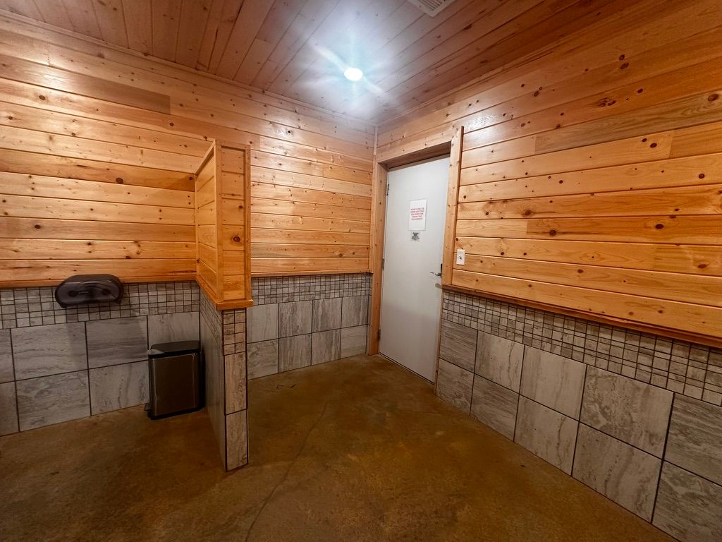 Small tiled utility room with wooden walls, concrete half-wall, sink, and a closed door under a ceiling light