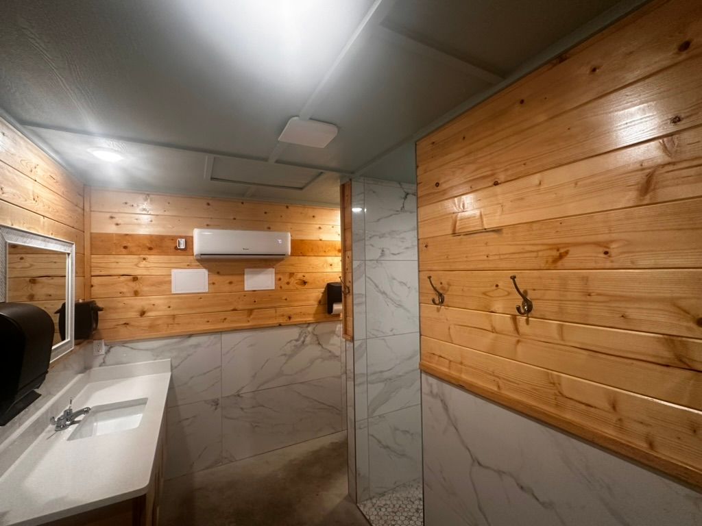 Modern bathroom interior with wood-paneled walls, marble tiles, a glass shower, and sinks