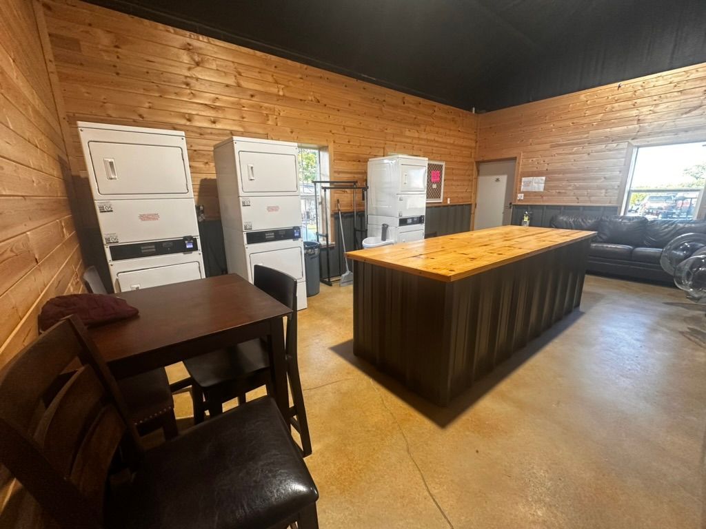 Rustic kitchen with wood walls, central island, dining table, and several refrigerators along the left wall