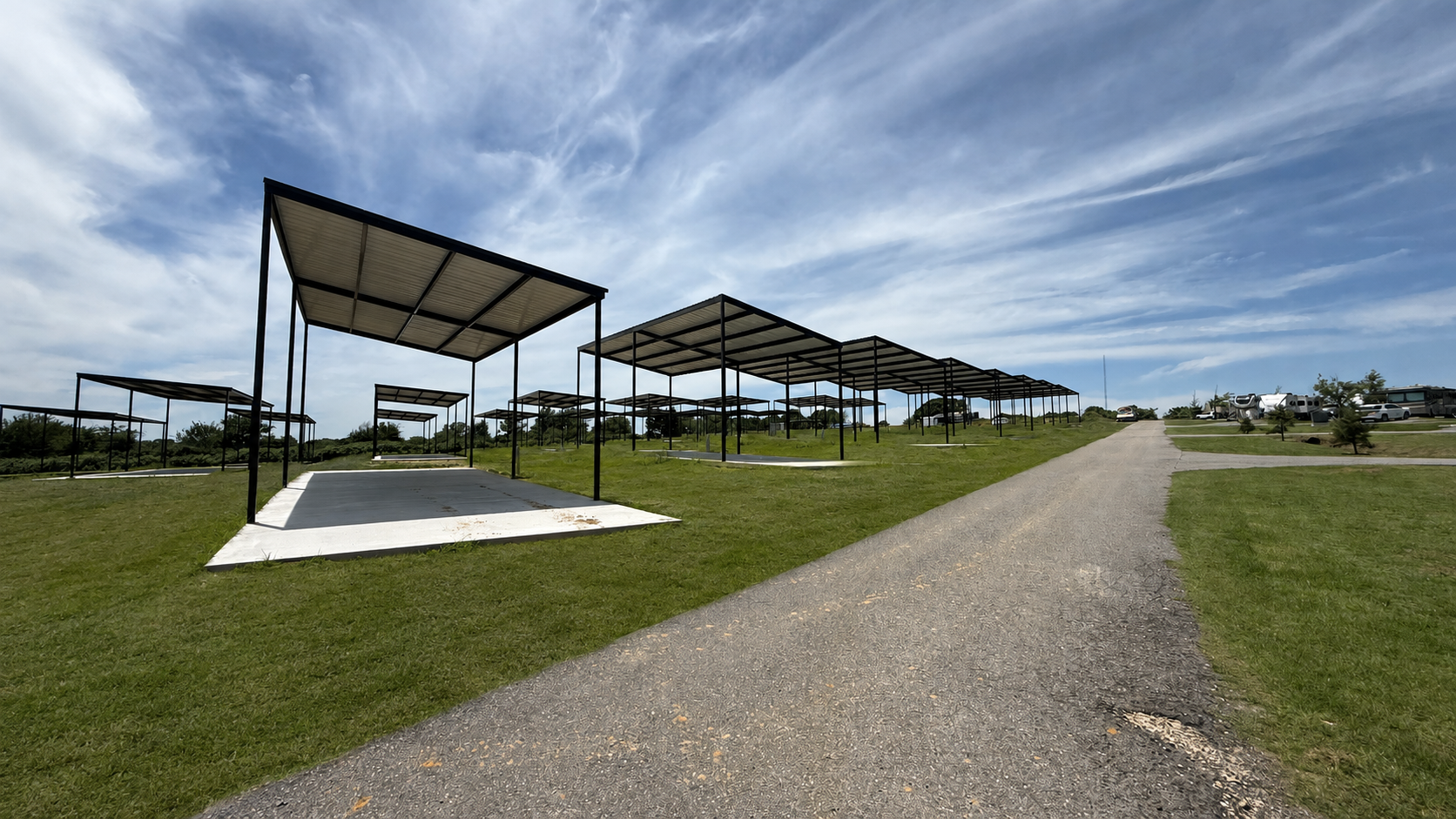 Rows of shaded picnic shelters beside a gravel path on a sunny grassy field