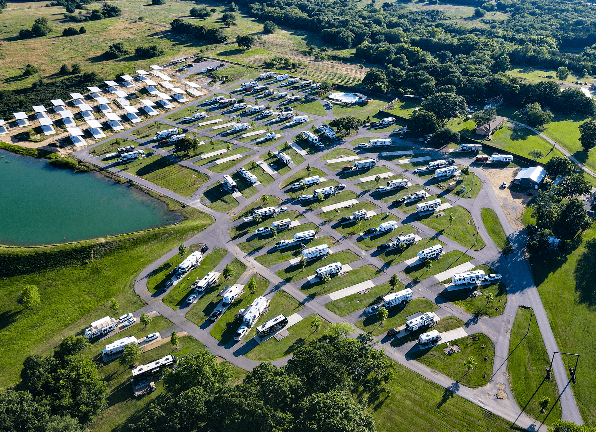 Aerial view of a crowded campground beside a lake, with rows of parked RVs and tents among green trees.