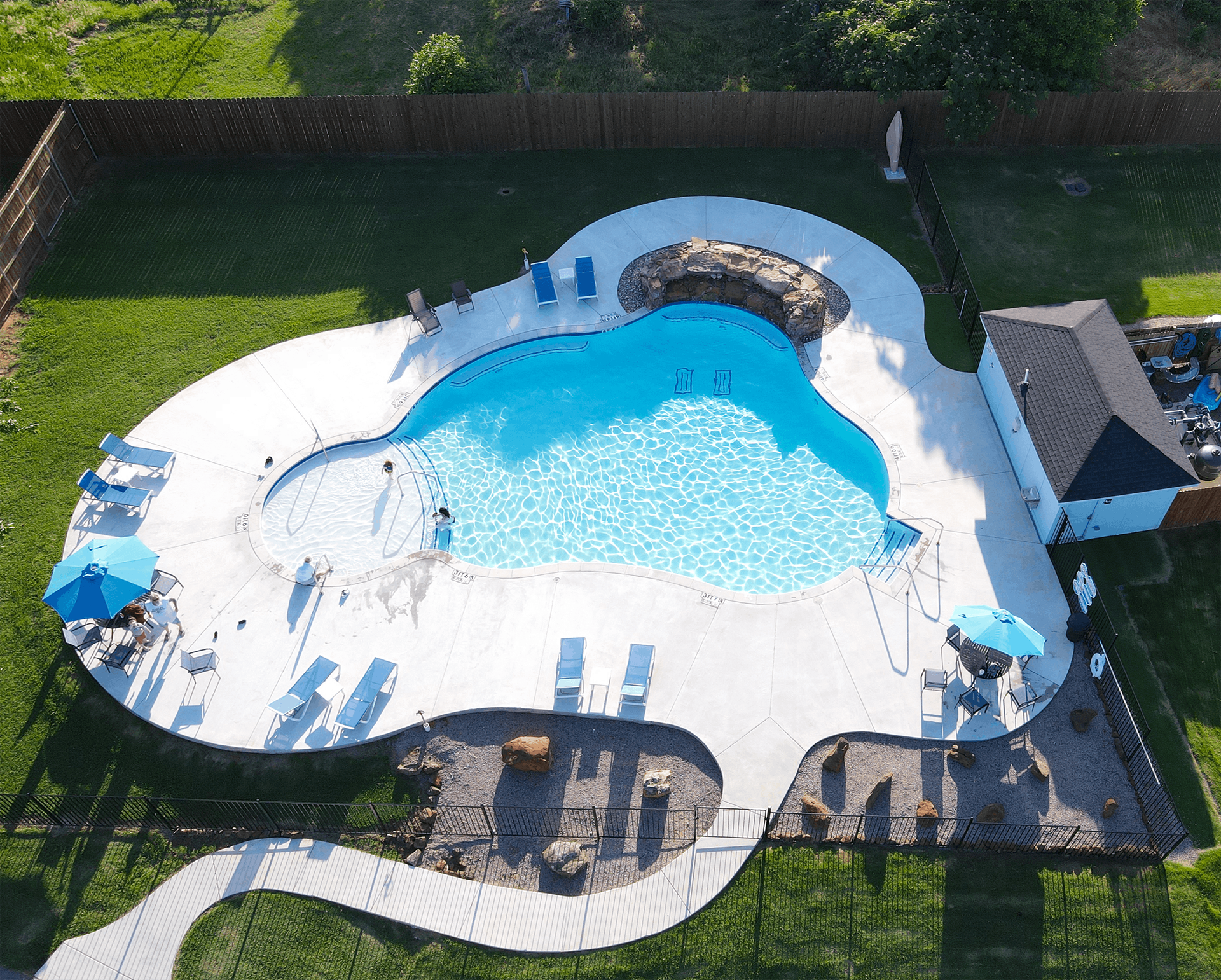 Aerial view of a backyard pool with blue water, white deck, and a rock waterfall feature.