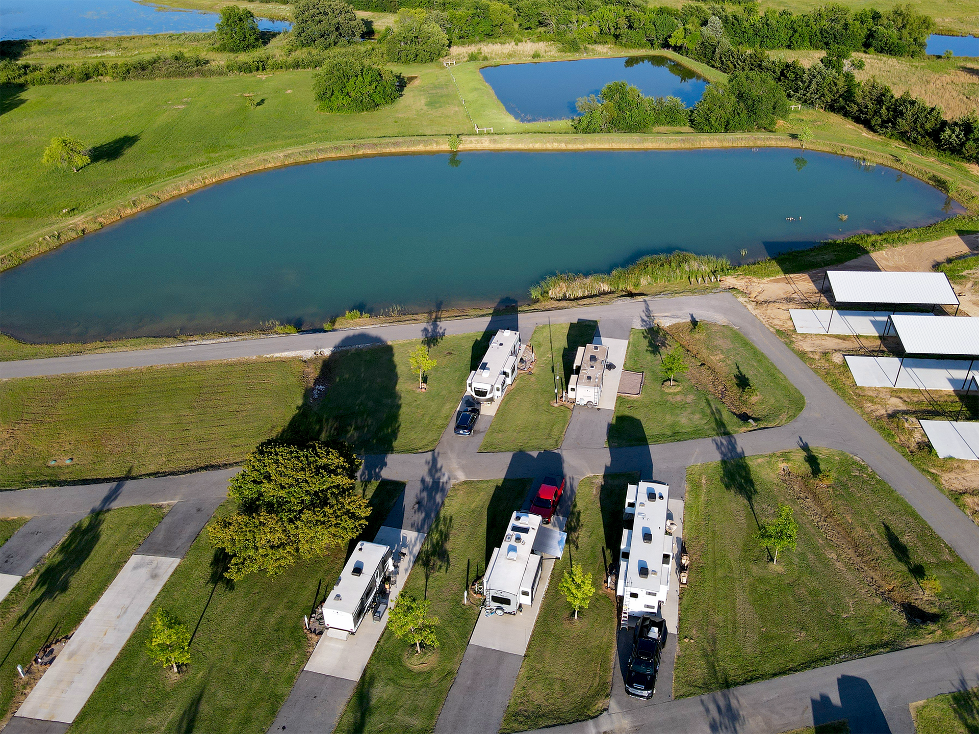 Aerial view of RVs parked beside a pond in a green campground with grassy fields and trees