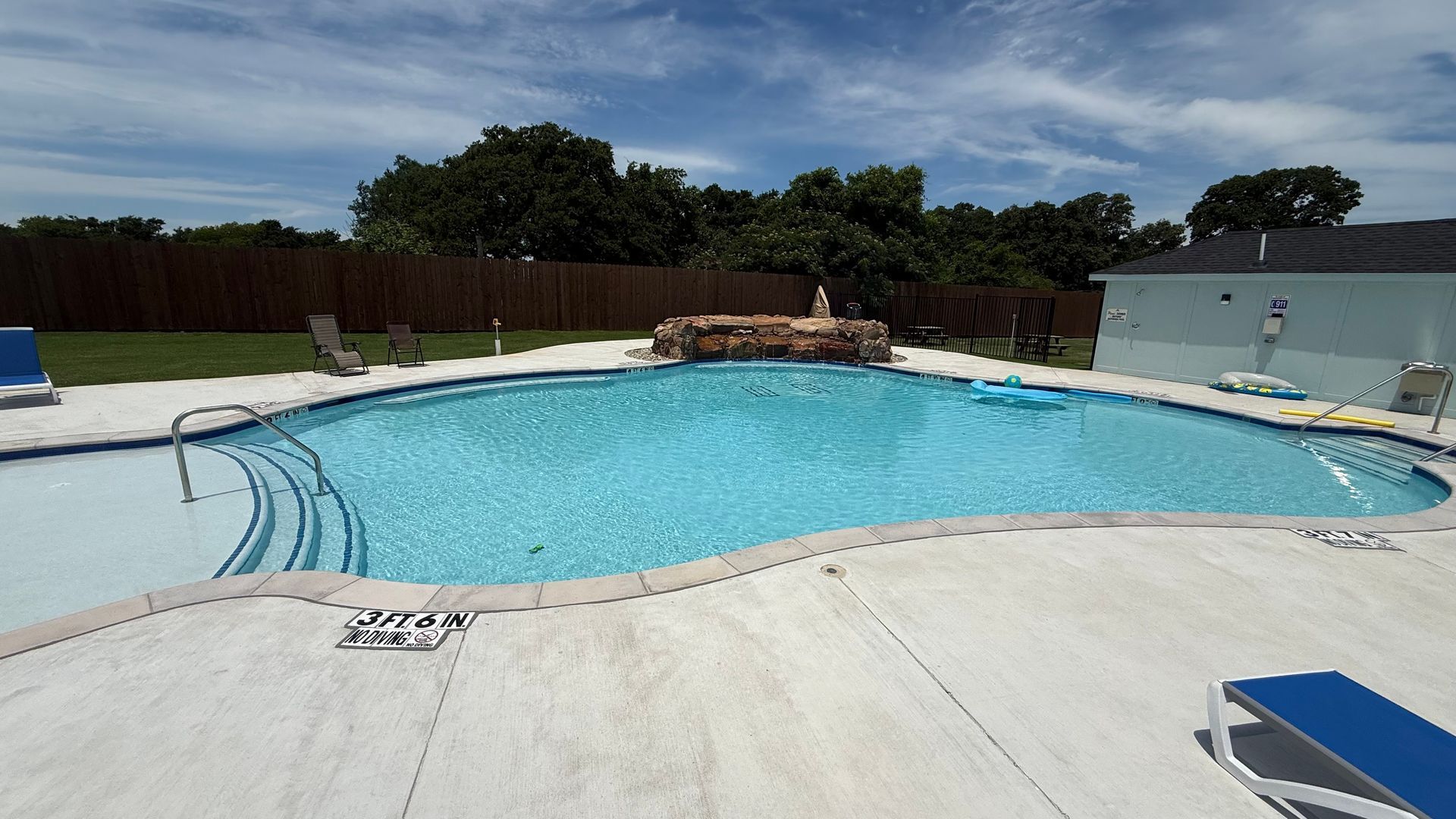 Outdoor swimming pool with clear blue water, concrete deck, and lounge chairs under a sunny sky