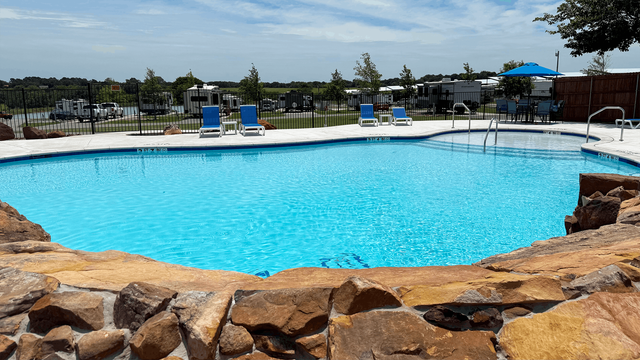Outdoor resort pool with bright blue water, stone edge, and lounge chairs under umbrellas
