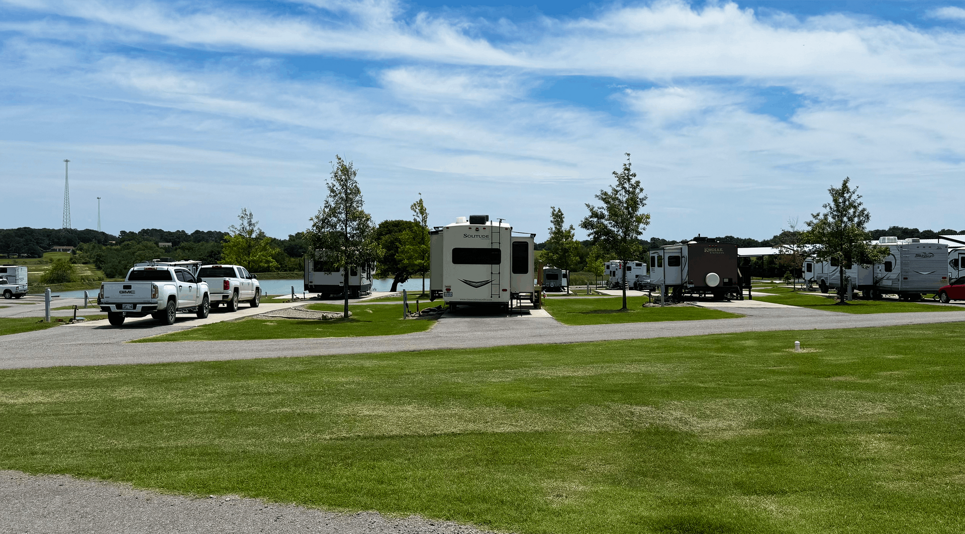 RVs and cars parked on a grassy lot under a blue sky.