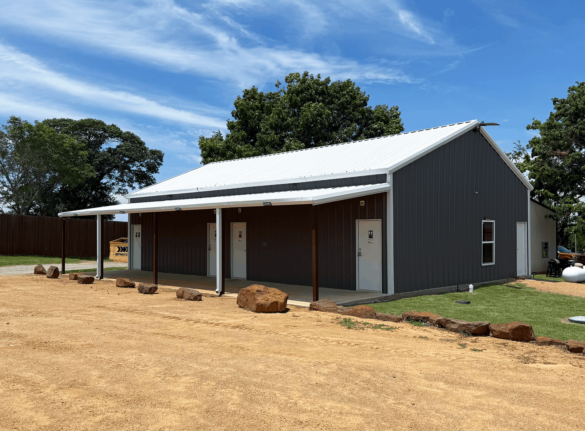 New gray house with white roof and porch, set on a dirt lot under a blue sky