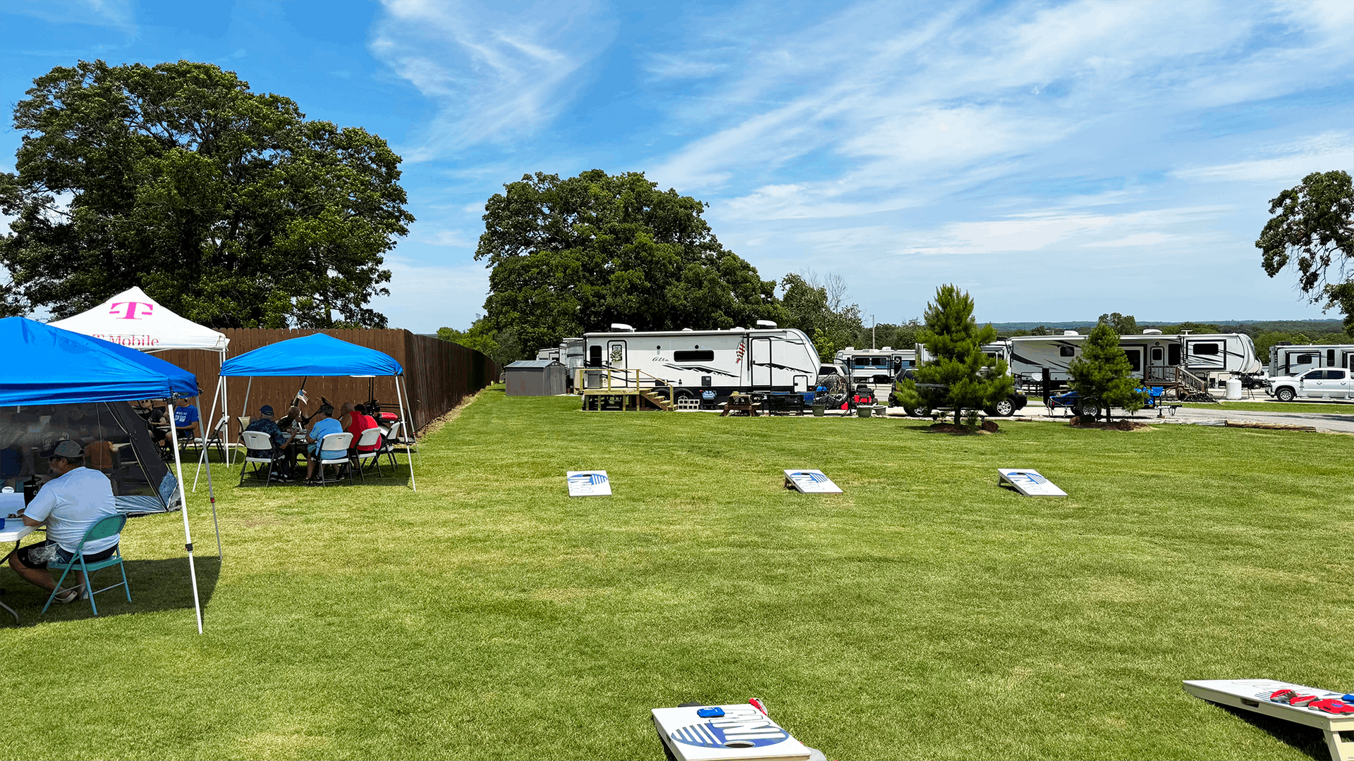 Outdoor festival on a grassy field with blue tents, picnic tables, and RVs under a sunny sky