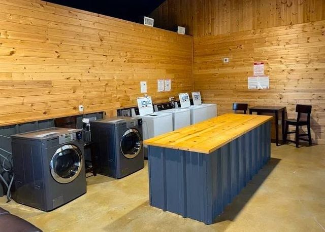 Laundry room with washers and dryers, wooden walls, and a central folding table