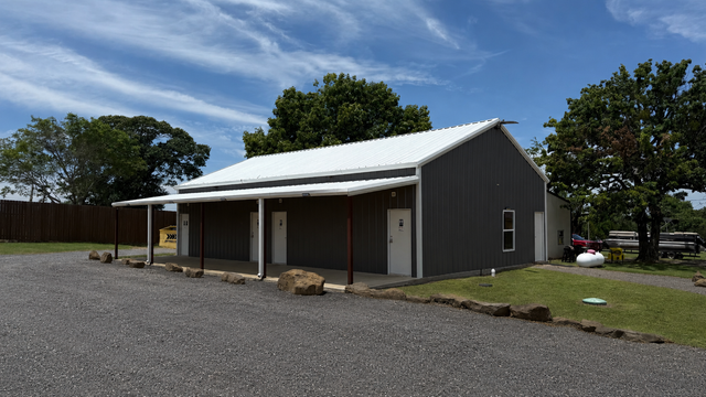 Gray barn-like building with a white metal roof on a gravel lot under a blue sky