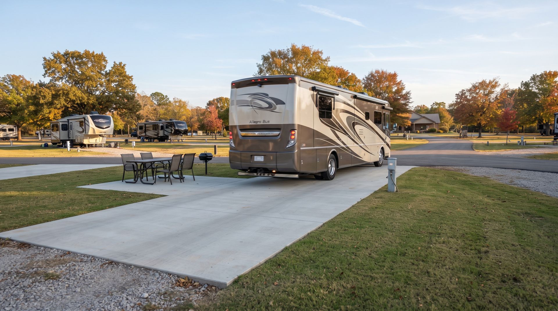 Motorhome parked on a concrete RV pad at a campground, with picnic table and autumn trees nearby