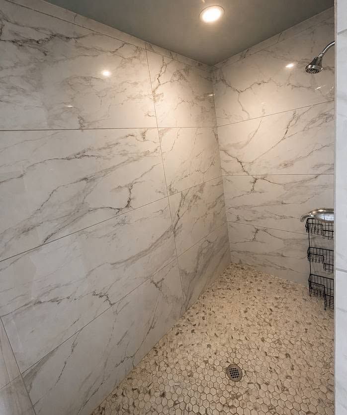 Empty marble-tiled shower with recessed light and pebble floor.