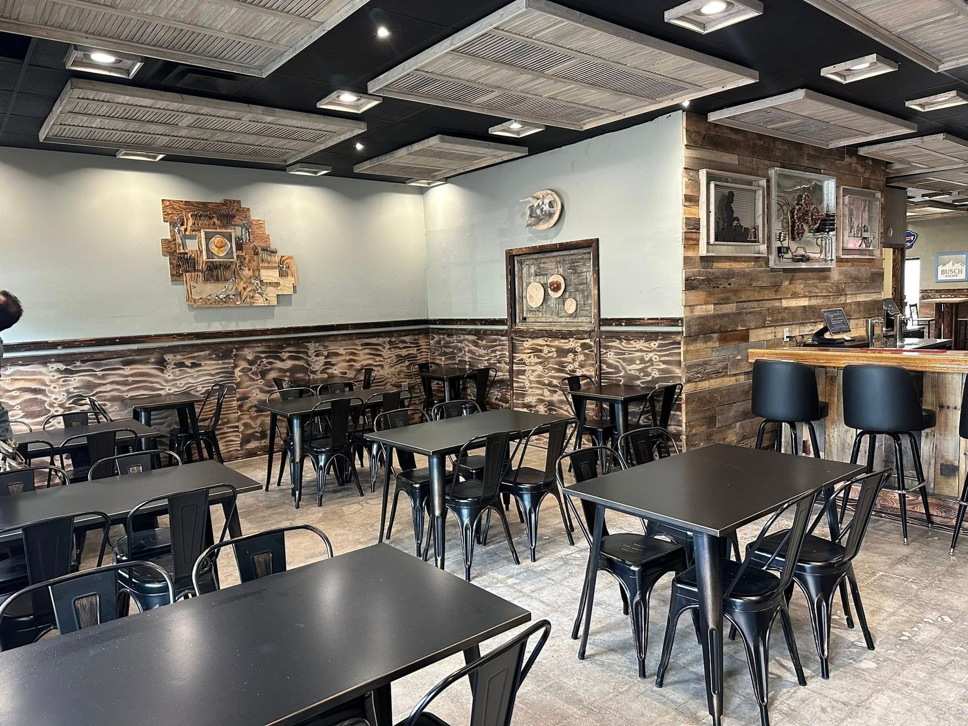 Restaurant interior with black tables and chairs, wood and brick walls, and textured ceiling.